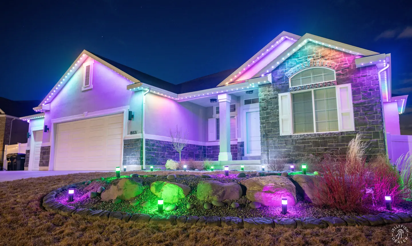Home with purple permanent roofline lighting and green landscape lights at night